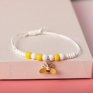 White braided bracelet with bee and sunflower pendant on a white shelf with pink background