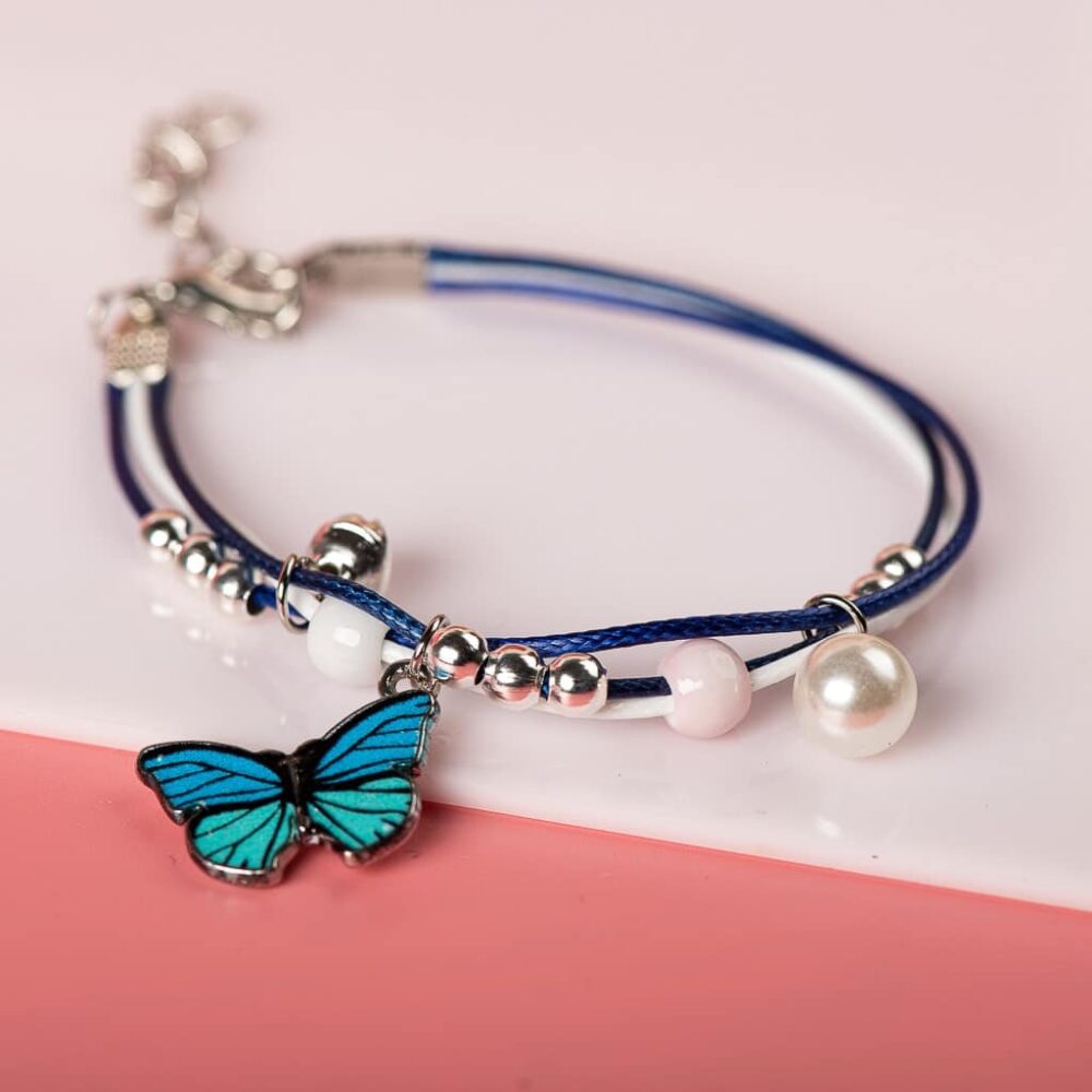 Bracelet with blue butterfly pendant with white pearls on white and pink background