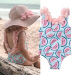 Girl's one-piece swimsuit with watermelon print on a beach, in the sand, in front of the sea