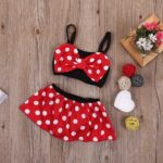Girl's two-piece bathing suit with bow tie in red minnie style on wooden background