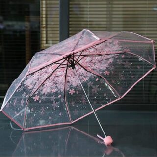 Transparent flower umbrella for children with pink border on a table in front of a window with closed curtains