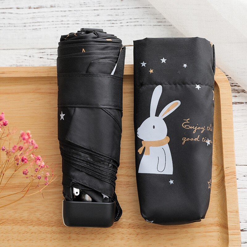 Mini children's pocket umbrella with white rabbit on black umbrella on wooden table