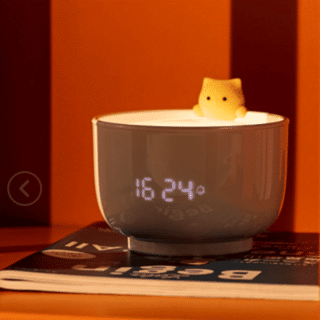 Nightlight in the shape of a teacup with alarm clock featuring a dedicated cat on a magazine and an orange background