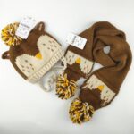 Brown and beige children's knitted hat and scarf with bird motif on a white background