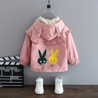 Solid color parka with rabbit pattern for pink children with black and yellow rabbit on the back, with white boots and a gray wall with wooden floor