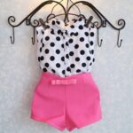 Pink shorts with white shirt printed with black polka dots on a black hanger