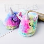 Children's rainbow unicorn slippers on a white table with soft fur
