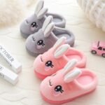 Grey and pink bunny ears slippers on white carpet with black eyes