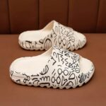 Comfortable summer flip-flops for all in white with black em pattern on a brown shelf