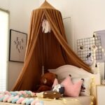 Tent-shaped bed tepee for cot on a bed in a room with pictures in the window