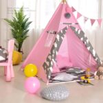 Small white and pink tepee for a child's bedroom with a green plant and balloons on the floor, with a pink chair