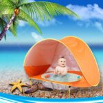 Orange children's beach tepee with baby inside on a beach with sea and palm tree
