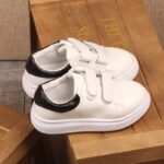 Casual flat sneakers for kids in white with laces on a wooden chair