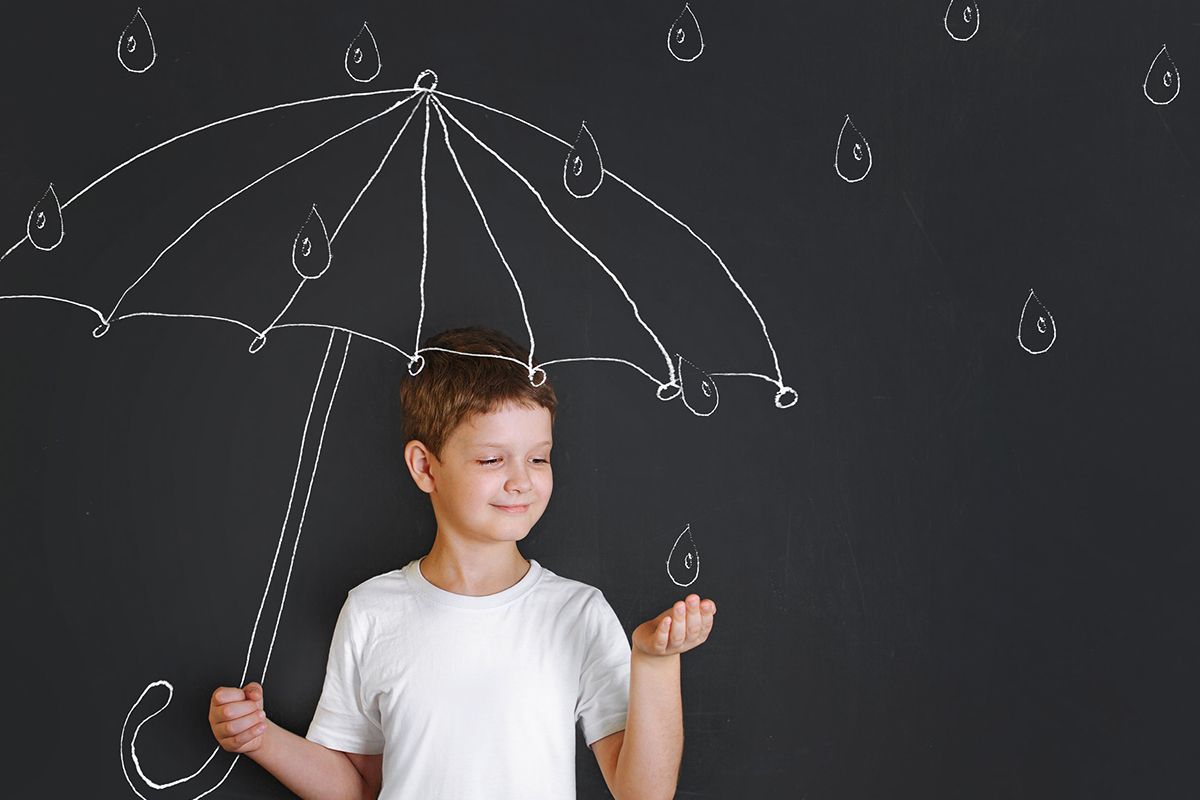 A young boy in a white T-shirt stands in front of a painting showing a child's umbrella and raindrops