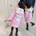 Long, shiny hooded bear jacket for girls in pink with bear in the hood and in the back on a girl in front of a mirror