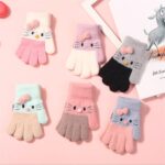 Cute and warm knitted winter gloves for kids with cute cat motif on pink background with book