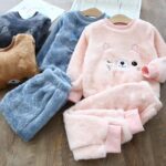 Pink and blue children's fleece pajama set with cat design on a wooden table