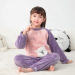 Flannel fleece pyjamas with a cute pattern for children in purple and pink on a girl in a white carpet with a cushion behind