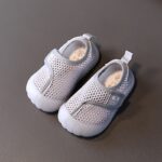 Children's beach shoes in gray mesh with a white rubber sole. They are set against a dark gray background.