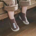 we see the legs of a seated child wearing brown socks with a white label