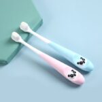 2 baby toothbrushes in pink and blue, laid flat on a green stand
